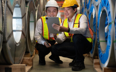 Industrial engineer and colleague wear safety helmet examining production in heavy steel engineering factory. Professional inspector and foreman worker inspecting material in manufacturing facility.